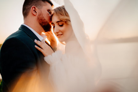 the bride and groom under the veil on the sunset by the riverの写真素材