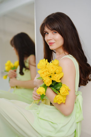 beautiful gentle young woman brunette with a bouquet of yellow tulips.の写真素材