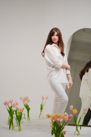 gentle brunette in white stands in a room with bouquets of tulips on the floor