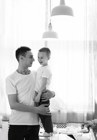 a cheerful cute little boy and dad in a white T-shirt and jeans in the kitchenの写真素材