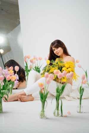 beautiful gentle young woman brunette with a bouquet of yellow tulips and mimosaの写真素材