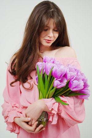 beautiful young brunette woman with long hair in pink with a bouquet of tulips.の写真素材