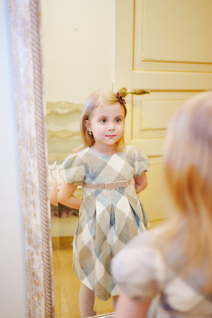 a cute little girl in a plaid dress looks in the mirror and primping.の写真素材