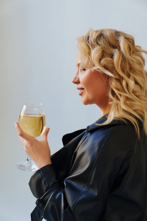 an attractive blonde in a black leather coat with a glass of champagne.の写真素材