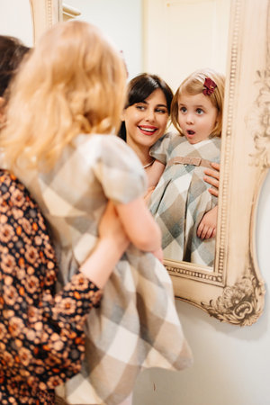 a cute little girl in a plaid dress and mom looks in the mirror and primping.の写真素材