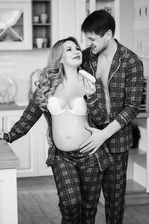 a pregnant woman and a man in pajamas eat cake in the kitchenの写真素材