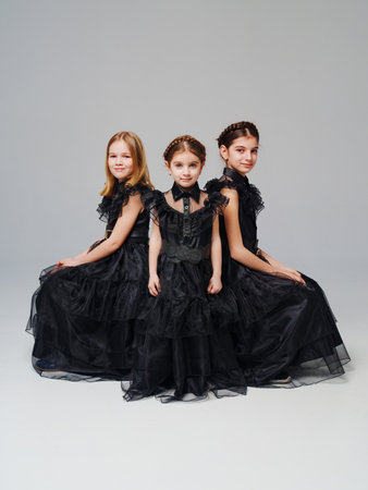 three cute girls in a black long curvy dress on a gray background.の写真素材