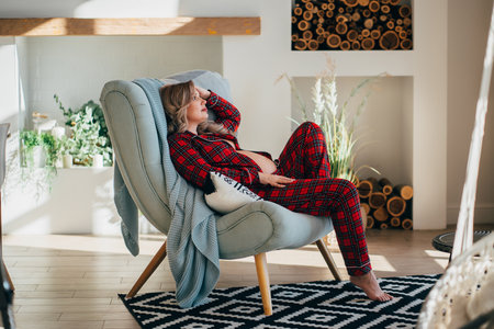 a pregnant woman topless in pajamas in the chair in a home interior.の写真素材