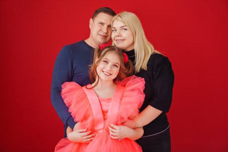 father, mother and daughter in a beautiful elegant dress on a red backgroundの写真素材