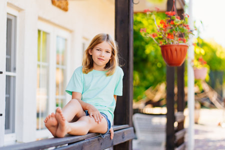 Cute sleepy girl sitting on the railing of the terrace of the house.の写真素材