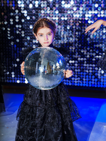 little girl with pigtail with mirror ball in a black long dress. shiny wallの写真素材