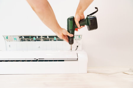 A man unscrews an air conditioner on the wall with a screwdriverの写真素材