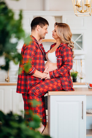 a pregnant woman and a man in pajamas in the kitchenの写真素材