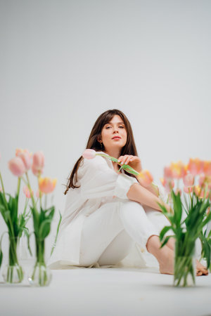 gentle brunette in white sits on the floor with vases of tulipsの写真素材