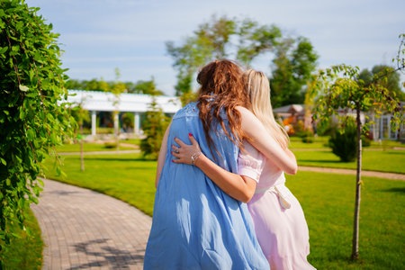 rear view without faces. Two women in blue and pink dresses hugging in the park.の写真素材