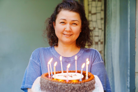 Middle-aged brunette woman with birthday cake with candles.