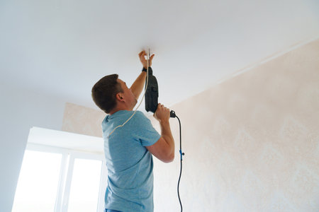 A man is working on the installation of a ceiling luminaire on the ceiling.の写真素材