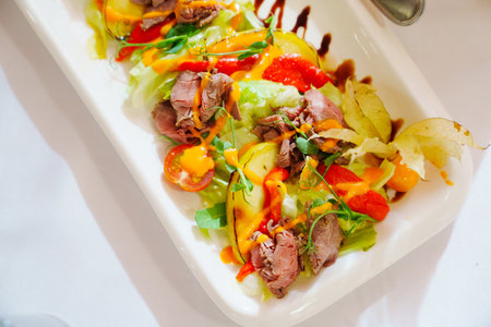 Meat salad with fruits and vegetables on a white rectangular plate.の写真素材