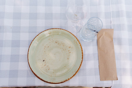 Empty plate, glasses and cutlery in a paper bag on a checkered tablecloth.