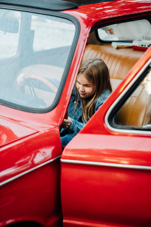 Teenage girl in denim clothes driving a red vintage retro car .