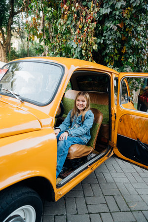 Teenage girl in denim clothes driving a yellow vintage retro car .の写真素材