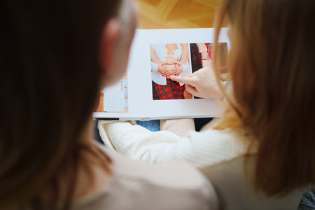 mother and daughter flips through a book with photos of dad and pregnant mom.の写真素材