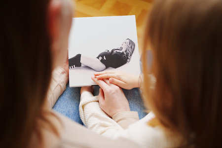 mother and daughter flips through a book with photos of dad and pregnant mom.の写真素材