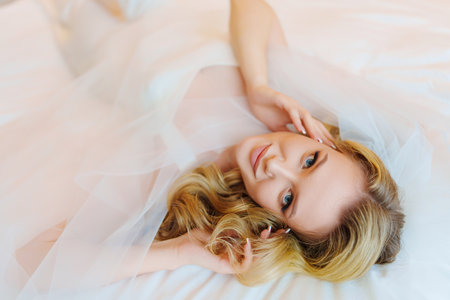 Morning of the bride. Delicate and beautiful blonde bride in bed under veil.の写真素材