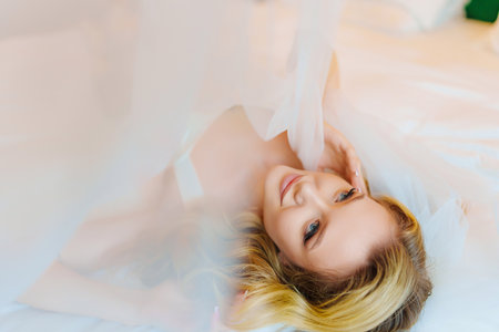 Morning of the bride. Delicate and beautiful blonde bride in bed under veil.の写真素材