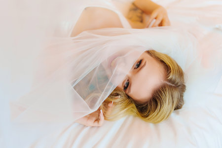 Morning of the bride. Delicate and beautiful blonde bride in bed under veil.の写真素材