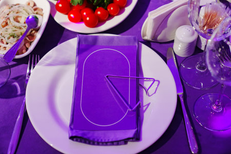 plate with napkin on a table set for holiday in purple in a dark banquet hall.の写真素材