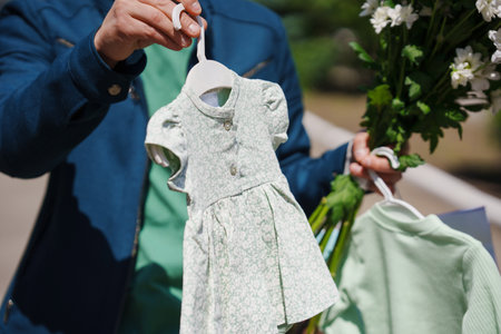 A man holds a small childrens dress and a bouquet of flowers.
