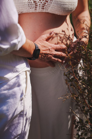 A man and a woman in white hold on to their pregnant belly.の写真素材