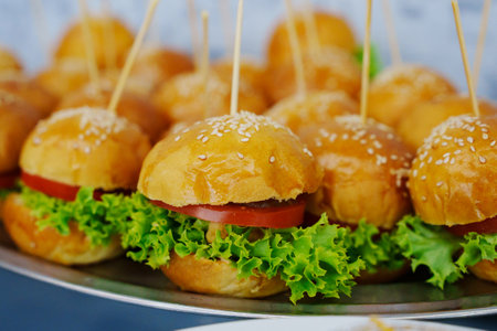 A plate of mini burgers with tomato and lettuce.