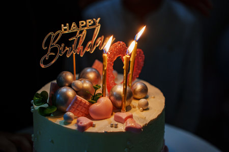 White and pink birthday cake with candles and chocolate decor.