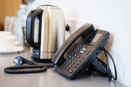 A corded black telephone in the hotel room on a table with a kettle and cups for guests. Comfort for guestsの写真素材