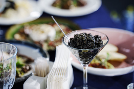 A glass with black caviar and a small spoon caviar. A delicacy fish dish for an expensive banquet.の写真素材