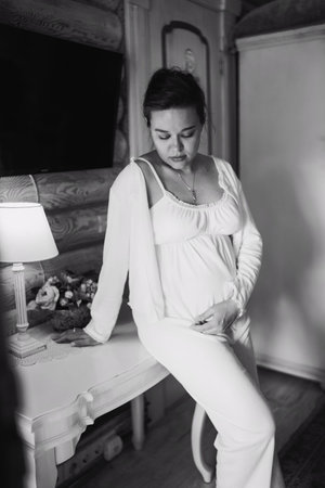 Calm and beautiful young pregnant woman in white pajamas in bedroom. comfortable home clothes. Healthy and happy pregnancy.の写真素材
