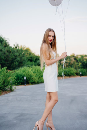 Beautiful slender blonde with long hair and balloons in an evening park.の写真素材