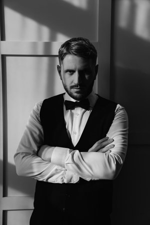 The groom in a waistcoat and tie bow against a white wall. black and whiteの写真素材