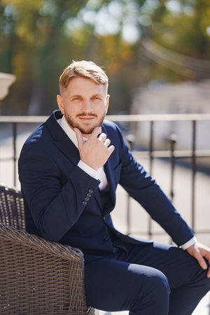 Attractive young blond man in suit sitting in chair outside.の写真素材