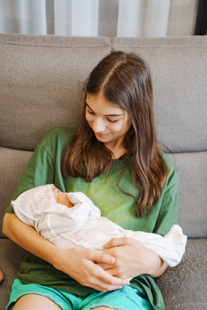 A teenage girl in green clothes holds a newborn sister in her arms.の写真素材