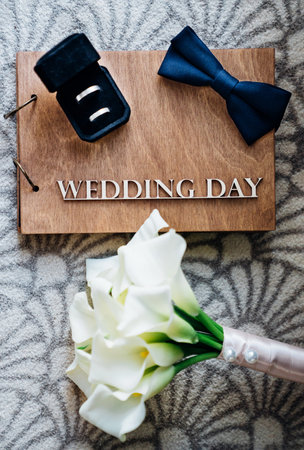 Grooms bow tie and wedding rings on a wooden folder and bridal bouquetの写真素材