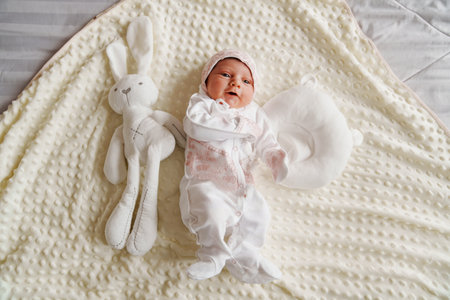Newborn baby in a hat with pink lace on the bed in the bedroom with a plush bunny. children's...