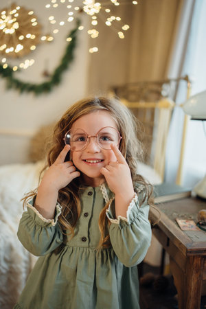 A beautiful little girl in a green dress and large round glasses. vision problems in children. glasses and lenses for reading.の写真素材