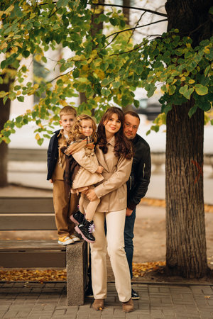 A family of four relaxes together on a sunny autumn day in a park. The parents with two children,...