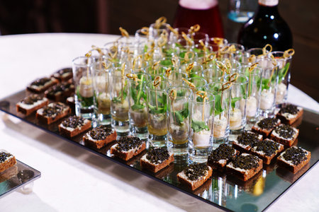 tray with sandwiches with black caviar and cups with canapes and white sauce.の写真素材