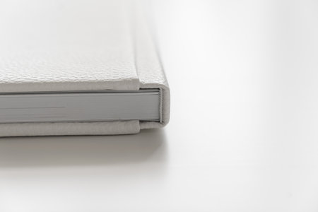 corner of the book in a white leather cover on a white table. binding for a photo album or book. storing printed photos in a book.の写真素材