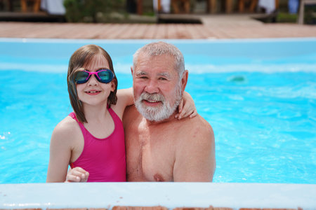 A grandfather and granddaughter play and swim in an outdoor pool.の写真素材