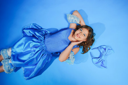 Cute teenage girl in blue doll dress with big blue bow posing lying on the floor. carnival and stage costumes. vocal and acting classes for children.の写真素材